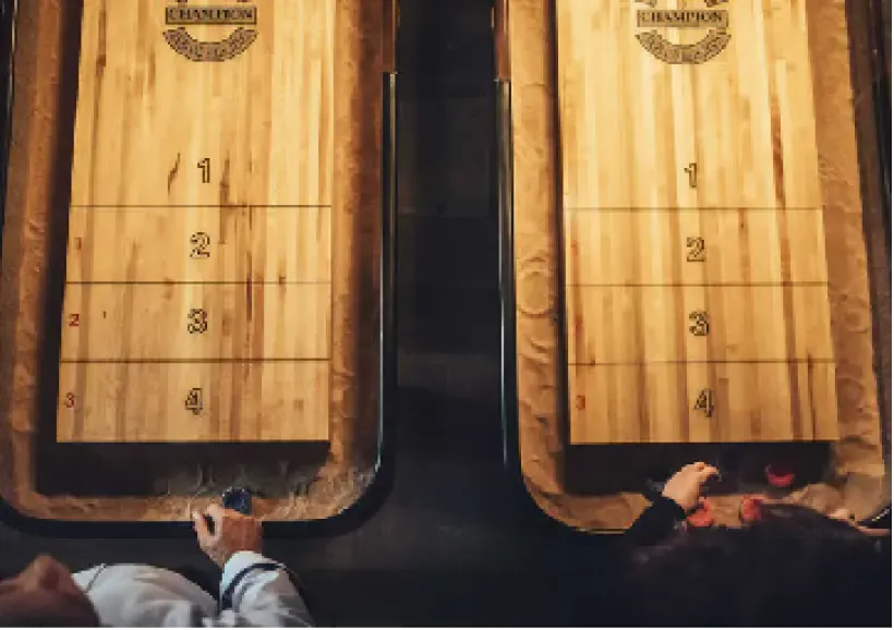 Two players facing off across a pair of shuffleboard tables