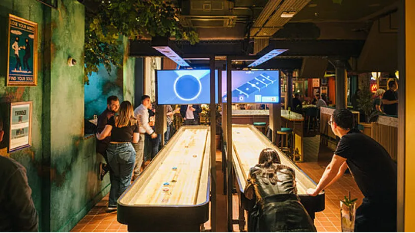 Guests playing on a curved shuffleboard table in a bar