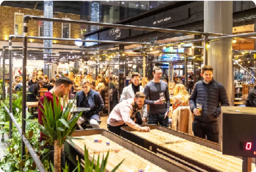 Guests playing shuffleboard in a busy covered market hall