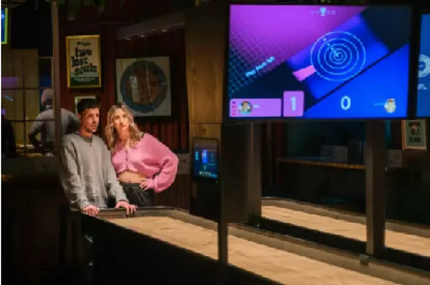 Two guests leaning on a SHUFL Tech table while the scoring screen shows their round