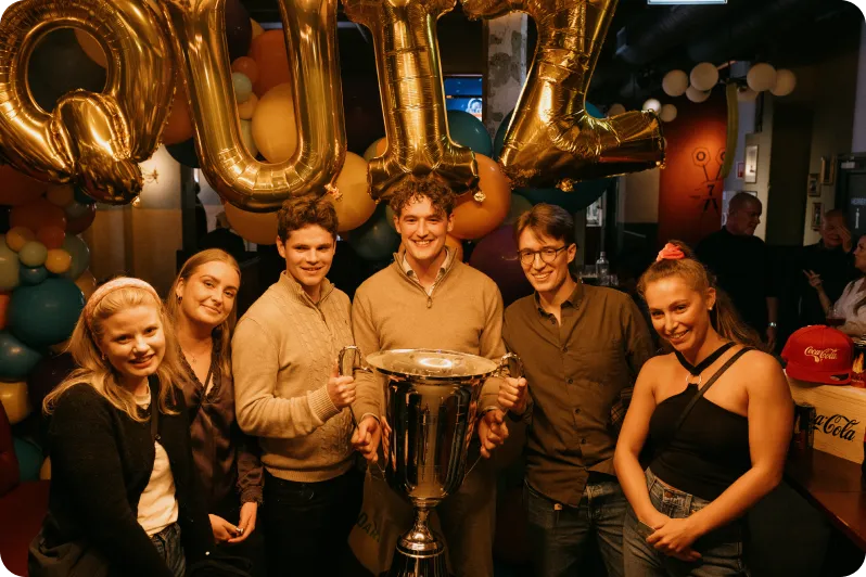 A group holding a trophy under gold balloons at a venue event