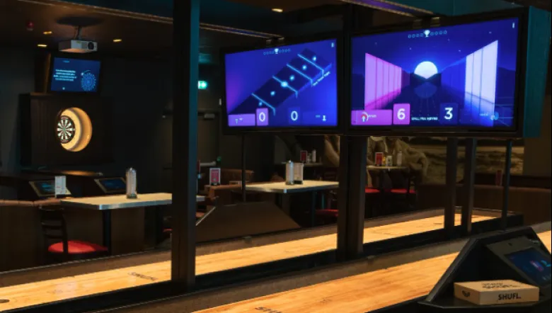 SHUFL Tech tables with overhead scoring screens in a games venue